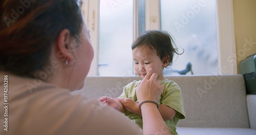 Foto Asian toddler patiently receives gentle facial application of skincare cream in a bright living room, focusing on pediatric dermatology, daily hygiene routine, and tender family bonding