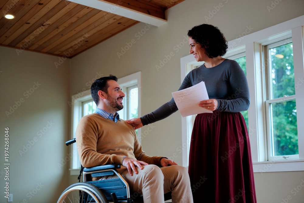 Fototapeta premium Medium shot of middle aged man with disability sitting in wheelchair while woman reviewing documents and supporting him, representing inclusive care. Useful for healthcare, insurance, accessibility