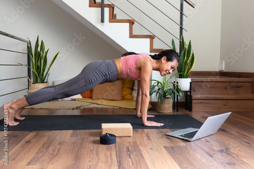 Foto Woman doing plank exercise watching online yoga class at home
