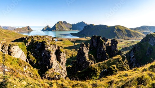 Expansive vista of rugged mountains beside a serene bay, with undulating grassy terrain and rocky outcrops in the foreground