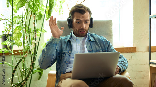 Man with headphones reacting surprised during online coaching call on laptop. Concept of client feedback, emotional response, remote consultation, and online coaching.