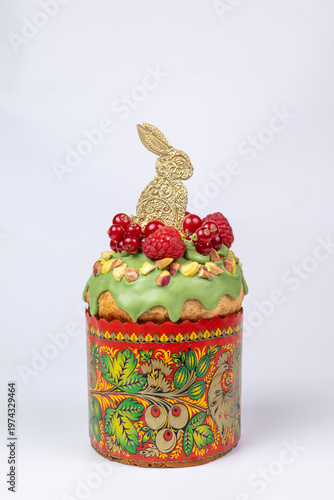 Easter Kulich in Decorated Paper Mold with Green Icing, Raspberries, Pistachios, and Golden Bunny