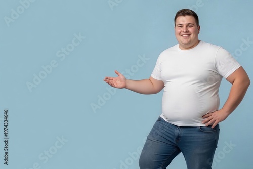 Man stands with one hand out and a smile in a blue room during daytime while wearing a white shirt and blue jeans