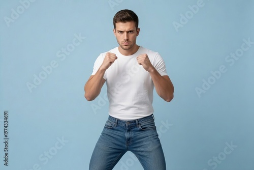 Person in white shirt and jeans stands in a fighting pose against a blue background during indoor photo session