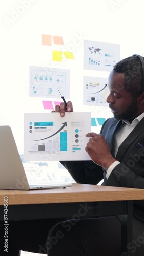 An African American man in a suit points to a financial graph during a virtual meeting, showcasing business growth and data analysis
