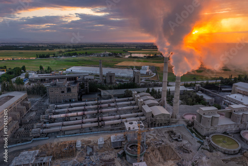 Aerial view of Industrial cement plant with smokestacks and agricultural fields at sunset