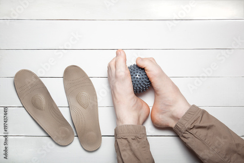 Top view of feet doing correction exercise with gray massage ball and orthopedic insoles