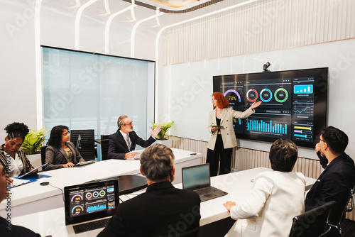 Professionals in a modern conference room review data dashboards on a large screen as a presenter leads a strategy meeting.
