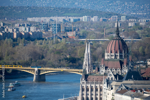 View of the Hungarian Parliament and the Danube in Budapest, with a bridge, boats and layered cityscape under clear spring light.