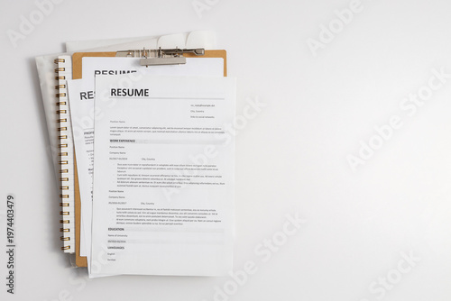Resume documents placed on a clipboard and stack of paper documents representing job search, candidate evaluation, and recruitment process
