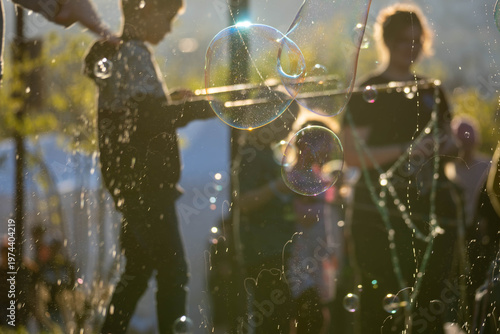 Soap bubbles and glittering spray drift through warm sunset light, with softly blurred people in the background, creating a dreamy festive atmosphere outdoors.