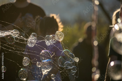 Close-up of shimmering soap bubbles drifting through warm sunset light, with a softly blurred crowd in the background, creating a dreamy outdoor atmosphere.
