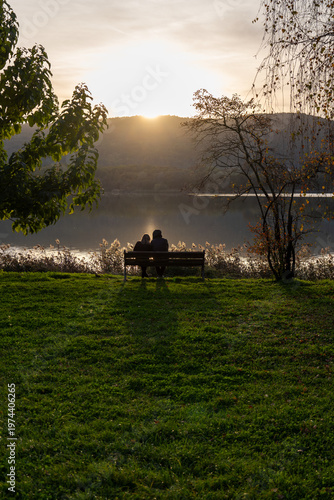 Romantic couple sitting on a bench at sunset by Comabbio Lake, Italy.