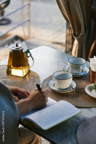 Woman writing in notebook at cafe table with tea and desserts