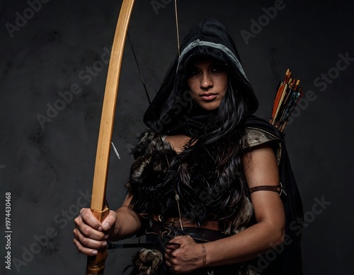 A person with dark hair, wearing a hooded cloak and carrying a bow and quiver of arrows, posing against a smoky gray backdrop
