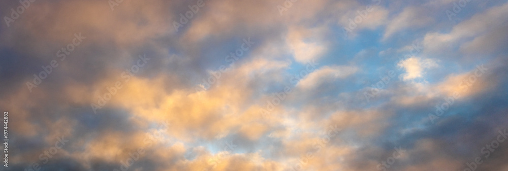 Obraz premium Dramatic evening sky with golden pink clouds against blue sky during sunset in panoramic composition