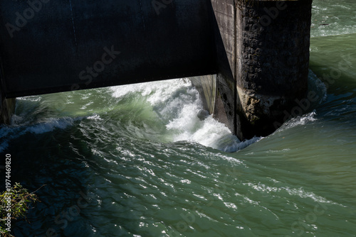Massive water discharge from a large dam with white foam and spray.