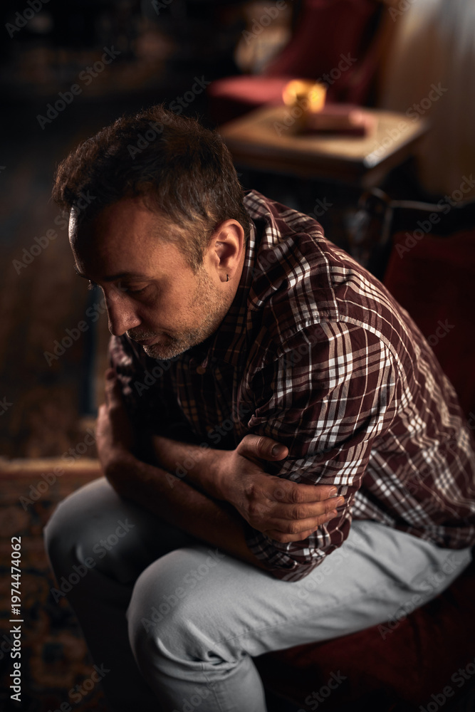 Obraz premium Man with headache, depression, sadness and loneliness sitting on a chair at home.