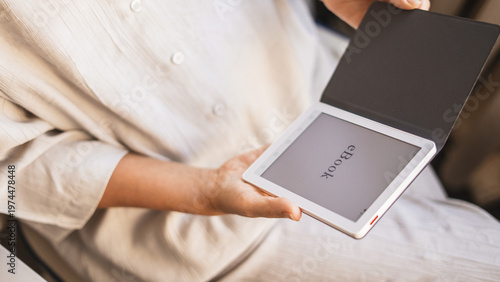 Woman holding ebook reader with cover in soft warm light at home. Concept digital reading, modern lifestyle, relaxation, comfortable learning, cozy atmosphere, mindfulness and peaceful leisure moment