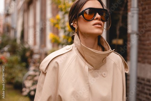 Close up portrait of a confident woman in a beige trench coat and vintage oversized sunglasses walking on a European city street, high fashion jewelry and luxury autumn outfit for urban lifestyle