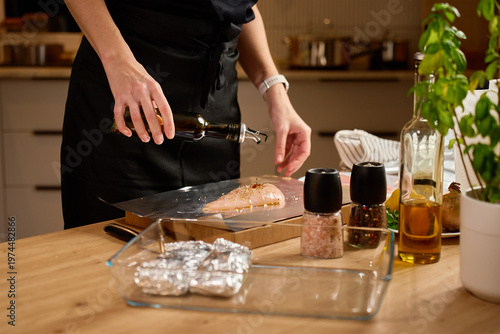Foto Close up of hands marinating raw chicken breast with soy sauce and spices on foil on wooden kitchen countertop