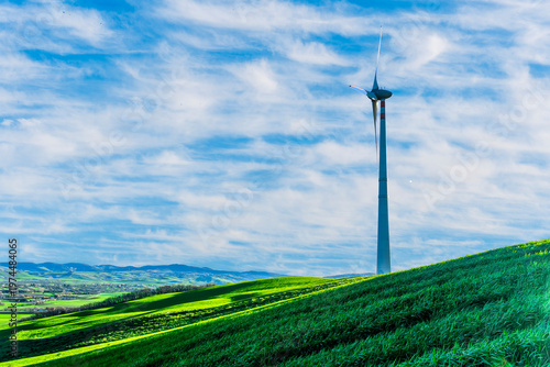 Fotografie wind turbines of wind power plant producing electricity on green sunset hills and cloudy sky on background of landscape