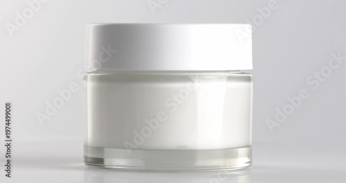 Glass jar with cosmetic facial cream, close-up footage on a rotating table.