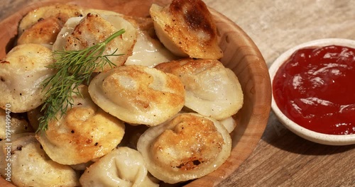 Wooden plate with freshly fried dumplings decorated with dill.