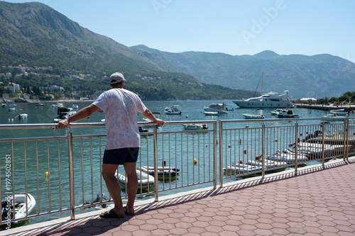 Young woman on the pier. Man looking at boats in the bay. Rear view. 
