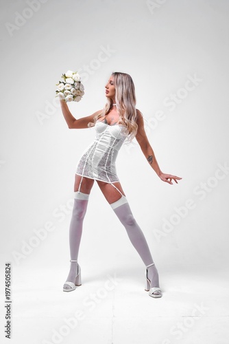 Gorgeous young woman holding bouquet wearing white lingerie stockings standing isolated on white background.