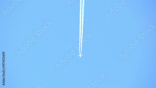 High-altitude commercial jet flying across a clear blue sky, leaving a long white contrail. Minimalist shot of aviation, travel, and atmospheric transport in bright daylight.