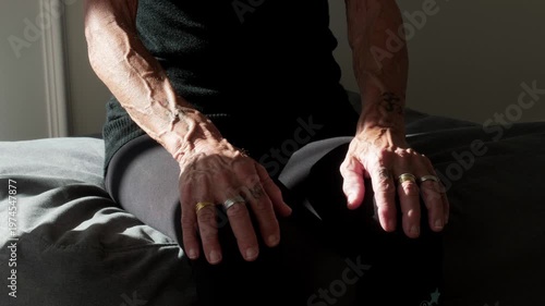 Close up of senior hands resting on knees in a seated position. Concept of contemplation, stillness, aging, patience, and peaceful reflection in a quiet home environment with soft light