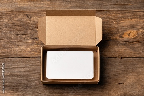An open cardboard box contains a blank white card, placed on a rustic wooden surface