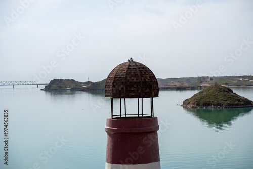 Solitary lighthouse on a pier surrounded by turquoise water. Qonayev, Central Asia