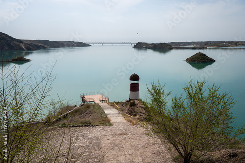 Solitary lighthouse on a pier surrounded by turquoise water. Qonayev, Central Asia