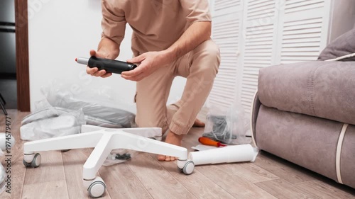 Man assembling office chair at home using tools. DIY furniture setup process in modern interior. Concept of home improvement, manual work, and comfortable workspace preparation.