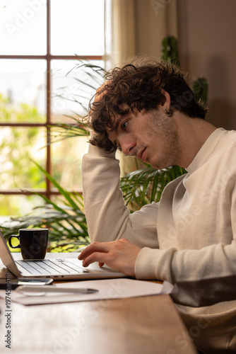 Jeune homme en situation de stress face à son ordinateur, illustrant la pression du télétravail et la fatigue mentale dans un environnement domestique lumineux.