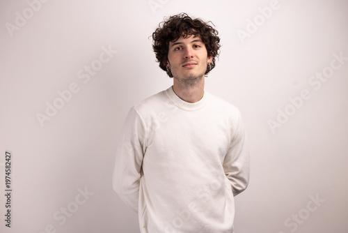 Portrait d’un beau jeune homme de 20 ans aux cheveux bouclés souriant sur fond blanc, exprimant confiance, naturel et simplicité dans un style minimaliste