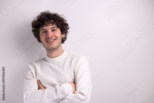 Portrait d’un beau jeune homme de 20 ans aux cheveux bouclés souriant sur fond blanc, exprimant confiance, naturel et simplicité dans un style minimaliste