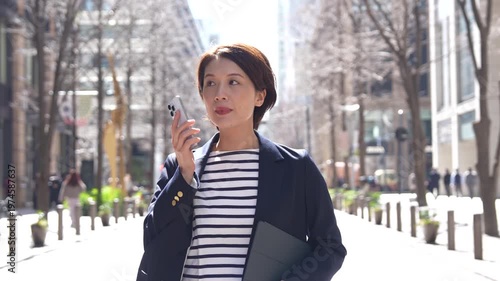 Japanese Businesswoman Walking and Talking on Phone in Spring City Street, Tracking Shot