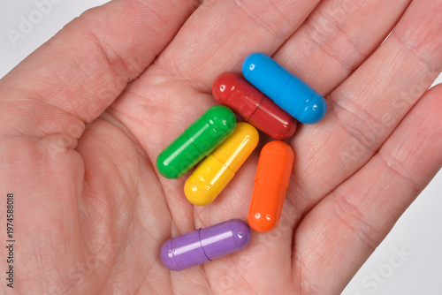 A close up top view of a human hand holding several bright multicolored pill capsules in a variety of vibrant rainbow colors