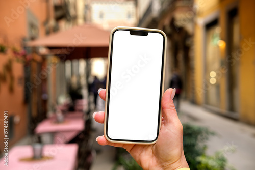 Smartphone mock up held by person wearing in outdoor cafe setting with tables and greenery in the background, smart phone with white blank screen mobile app design and advertising, online marketing