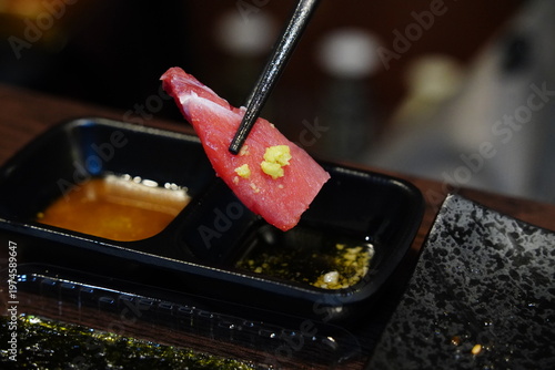 close-up photo of a piece of fresh tuna sashimi picked up with chopsticks.