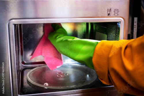 Woman cleaner wipes inside of microwave oven with pink cloth. Kitchen appliance maintenance and professional cleaning service.