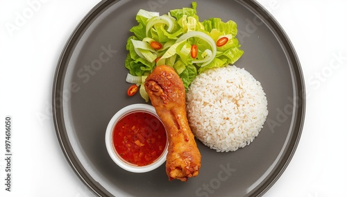 Breakfast idea featuring a crispy fried chicken leg, rice, lettuce, and chili sauce on a grey plate against a white background. Aerial perspective.
