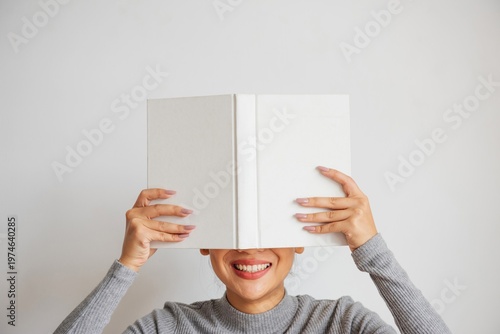 Obraz na plátne Smiling woman hiding behind book