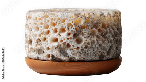A close-up view of a unique porous stoneware vessel on a wooden base against a black background