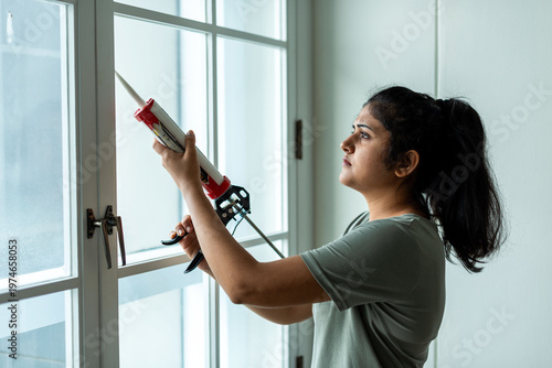 Fotografi Woman sealing window with caulk