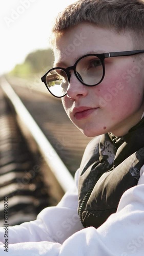 A young man in glasses sits sadly on a railway track, symbolizing loneliness and despair. The scene reflects the emotional impact of school bullying.