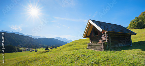 wooden shelter at green alpine pasture, bright sun with sunbeams, Wetterstein alps